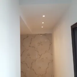 Korytarz z obniżonym sufitem i wbudowanym oświetleniem punktowym, ściany wykończone płytkami imitującymi marmur.