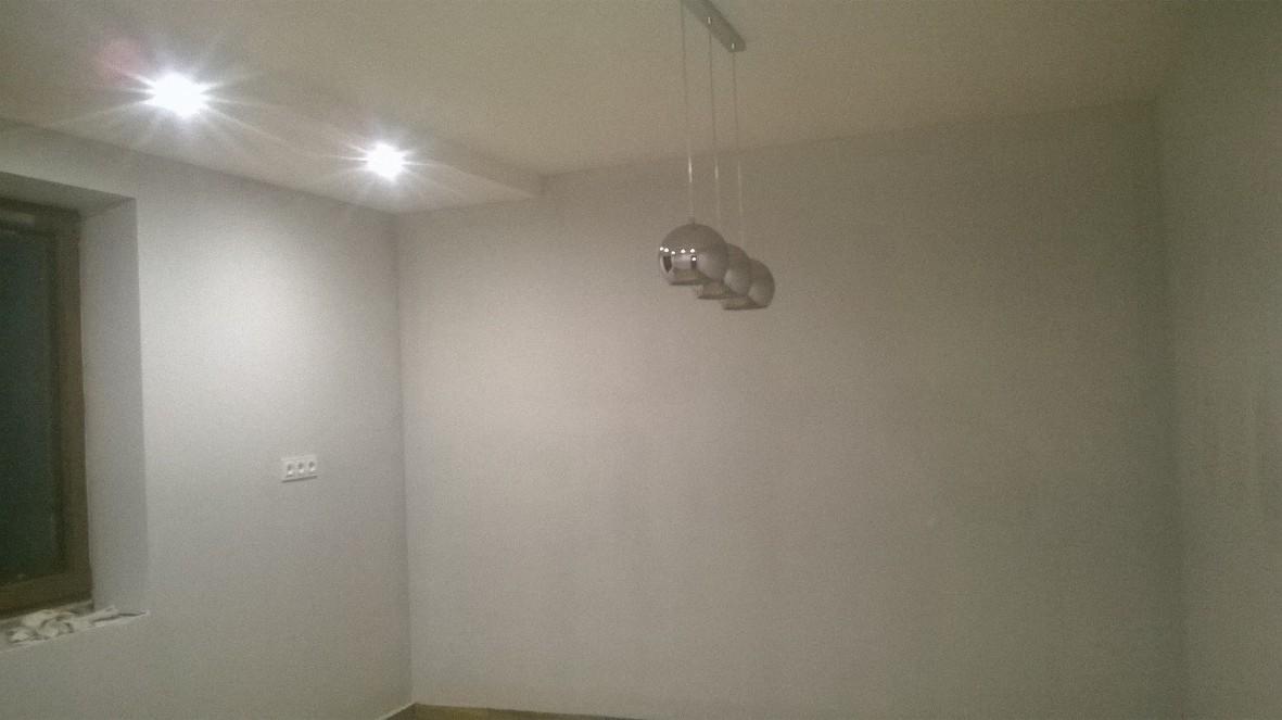 Świeżo pomalowane, jasnoszare ściany w pustym pokoju z trzema okrągłymi lampami wiszącymi i dwoma punktowymi źródłami światła w suficie.