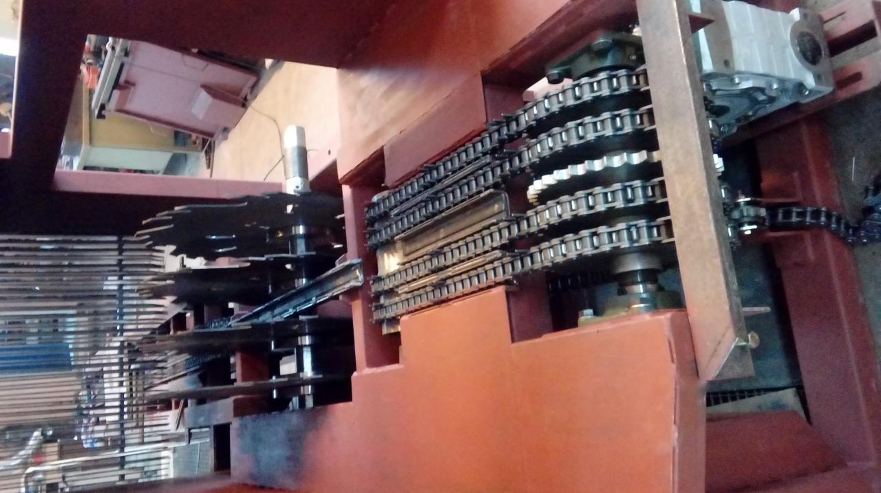 Widok z góry na mechanizm z łańcuchami, zębatkami i elementami konstrukcyjnymi w kolorze ceglastym, prawdopodobnie część maszyny CNC.