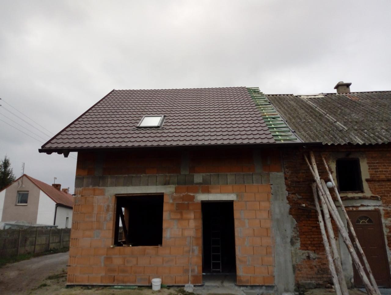 Dom w trakcie wymiany pokrycia dachowego: część dachu z brązowej blachodachówki z oknem dachowym, część ze starego eternitu, widoczne łaty pod nowe pokrycie.