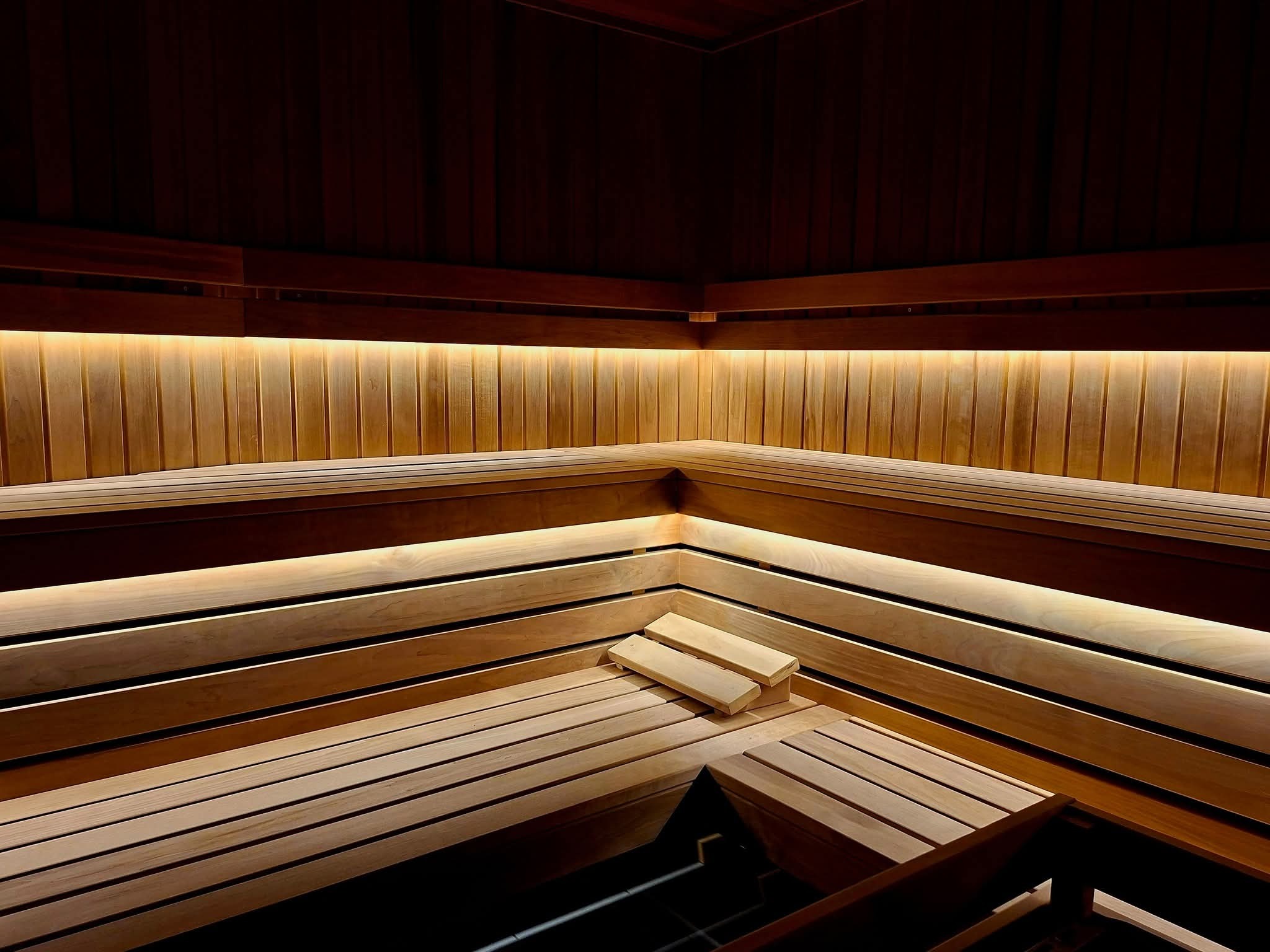 Wnętrze sauny z drewnianymi ławkami i podświetleniem LED, ukazujące ciepłą atmosferę i dbałość o detale wykończenia.