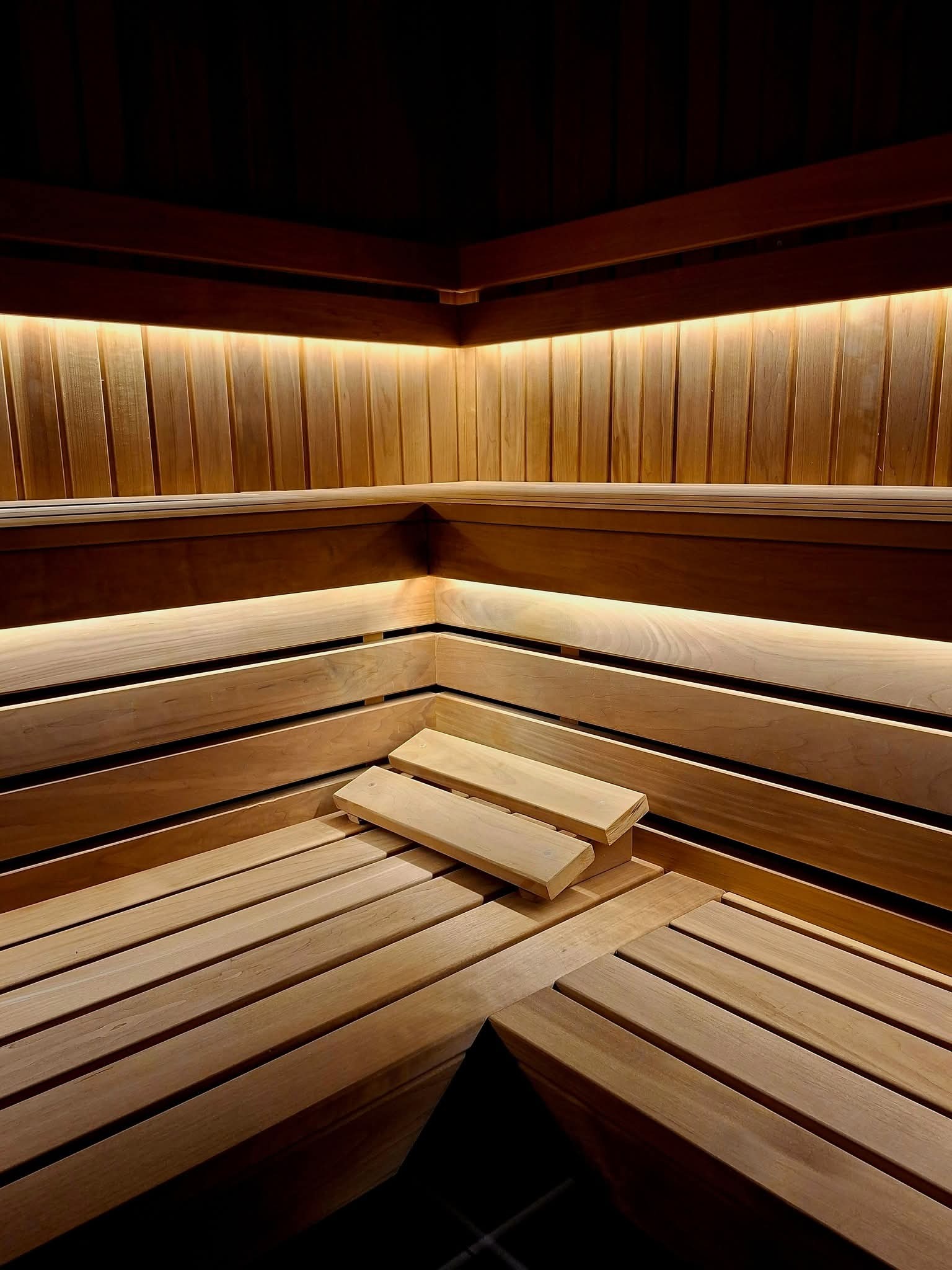 Drewniane wnętrze sauny z podświetleniem LED, ukazujące ławy i boazerię w ciepłym odcieniu drewna. Minimalistyczny design z akcentem na naturalne materiały i subtelne oświetlenie.