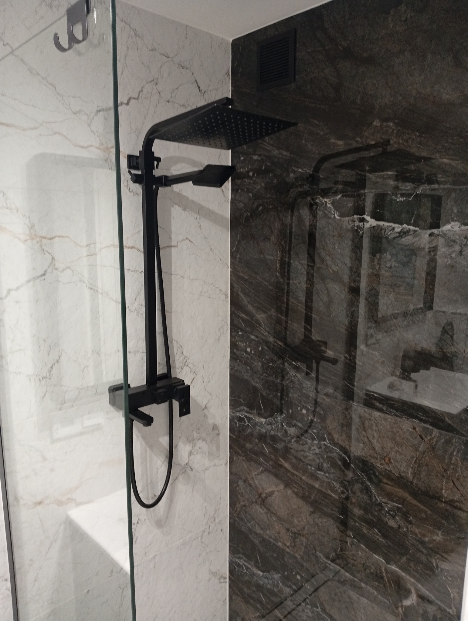 Nowoczesna kabina prysznicowa z czarną armaturą i marmurowymi płytkami w odcieniach bieli i szarości. Minimalistyczny design, eleganckie wykończenie.