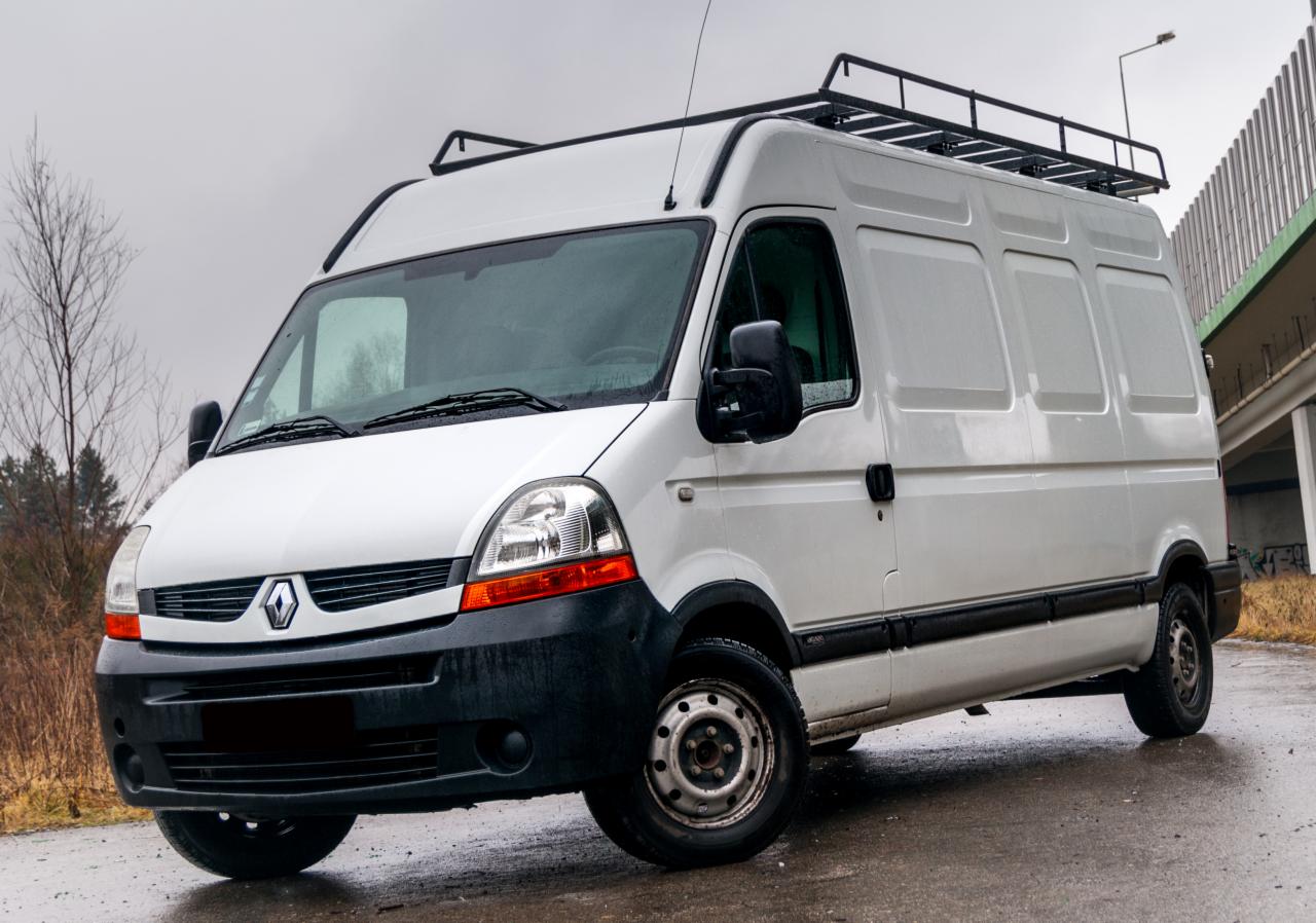 Bielsko-Biała: Biały bus Renault Master z relingami dachowymi, zaparkowany na mokrym asfalcie, widoczny z niskiego kąta.