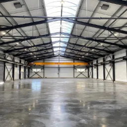 Wnętrze hali produkcyjnej z suwnicą podsufitową ZBUD, widoczne stalowe elementy konstrukcji, świetliki dachowe i posadzka przemysłowa.