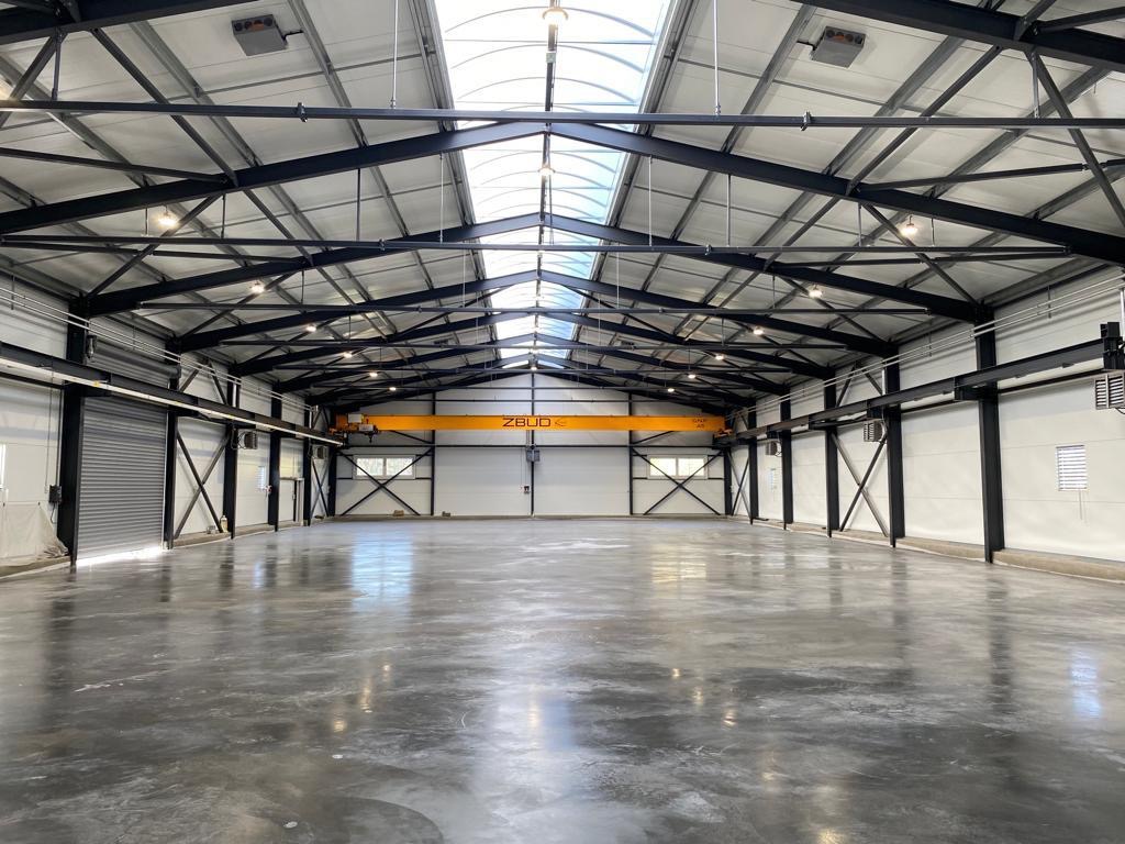 Wnętrze hali produkcyjnej z suwnicą podsufitową ZBUD, widoczne stalowe elementy konstrukcji, świetliki dachowe i posadzka przemysłowa.