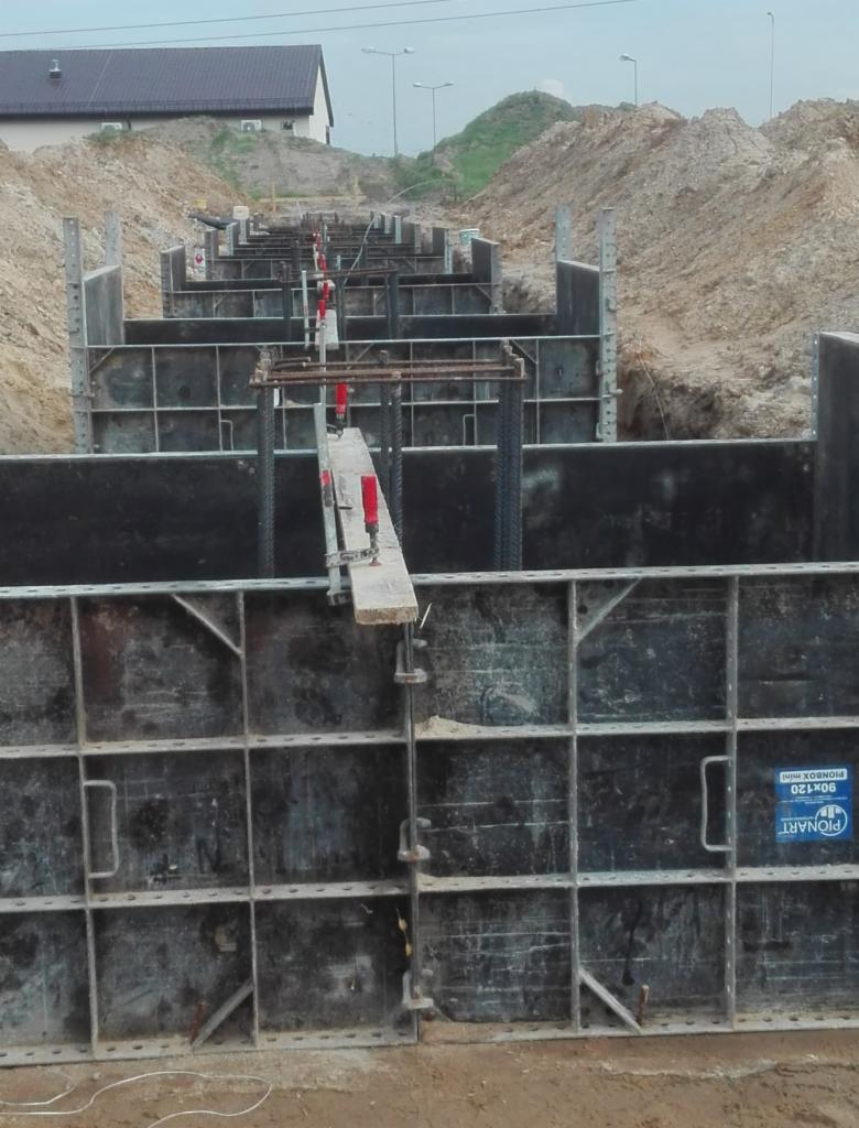 Szczegółowe ujęcie szalunków pionowych w wykopie pod fundamenty, z widocznymi elementami zbrojenia i deskowaniem, przygotowane do betonowania.