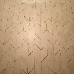 Perfectly Home - Ściana wyłożona beżowymi płytkami w jodełkę, widoczny element do poziomowania płytek w prawym górnym rogu.