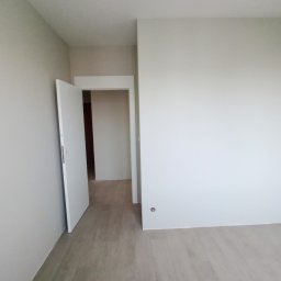 Perfectly Home - Pomalowane na jasny odcień wnętrze pokoju z otwartymi białymi drzwiami i panelami podłogowymi w odcieniach beżu i szarości.