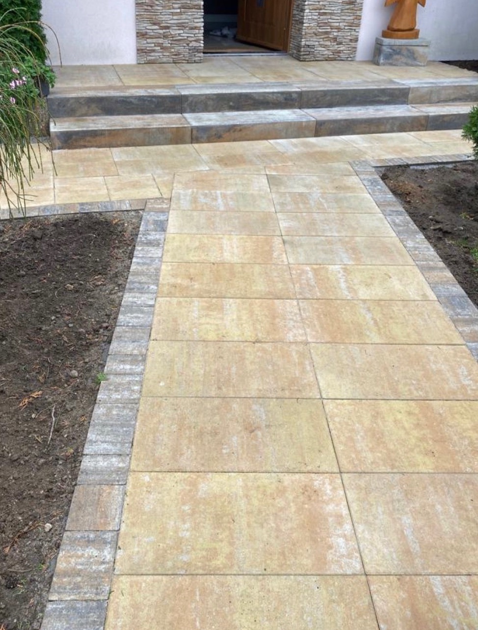 Żółta kostka brukowa ułożona jako ścieżka prowadząca do wejścia do domu z kamiennymi schodami i obrzeżem z szarej kostki, widok z góry.