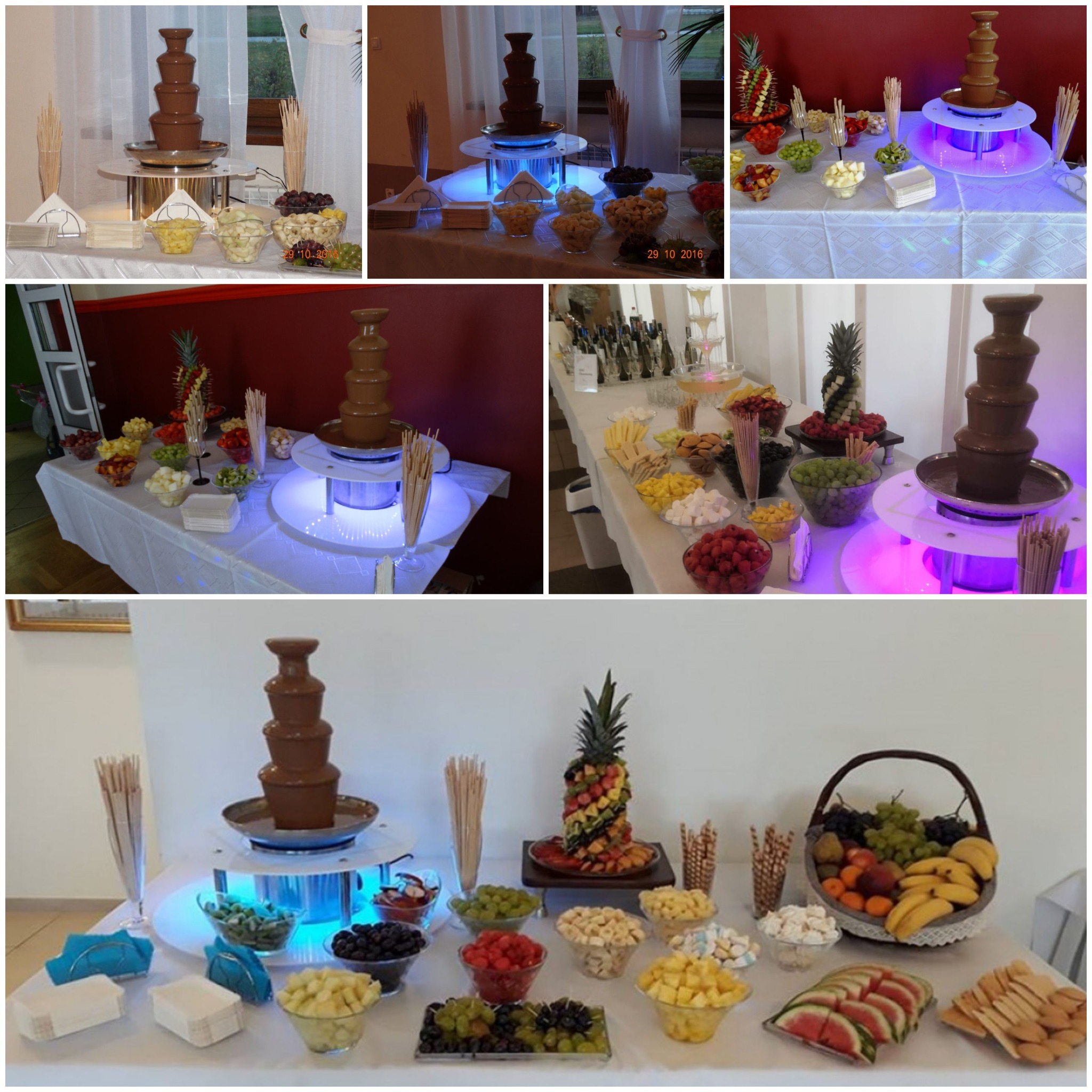 Stół z fontanną czekoladową otoczoną miseczkami świeżych owoców, w tym ananas, winogrona, banany, arbuzy i pianki, na białym obrusie z dekoracyjnym podświetleniem.