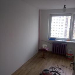 Rafał i Remonty - Pomieszczenie po malowaniu ścian na biało, widoczny odkurzacz, grzejnik pomalowany na fioletowo, wiadro farby i taboret.