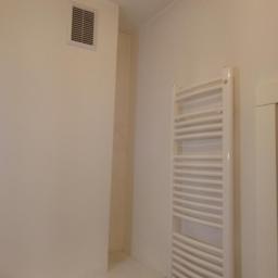 Rafał i Remonty - Ściana w łazience po malowaniu na jasny kolor, widoczny grzejnik drabinkowy i kratka wentylacyjna.