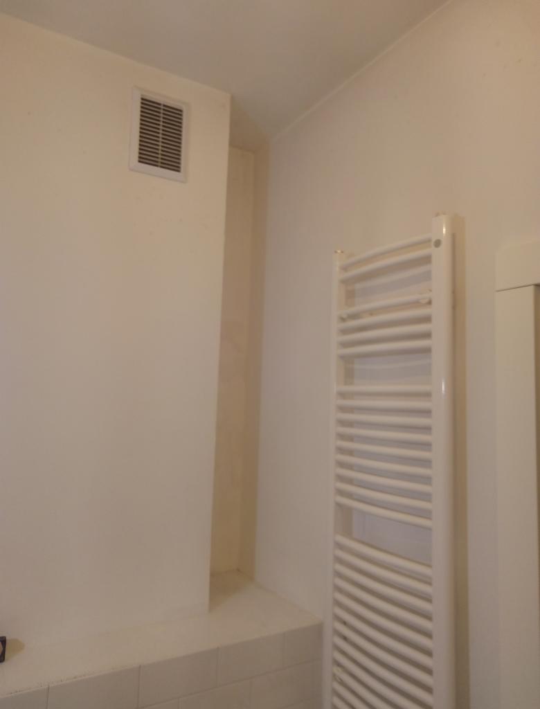 Ściana w łazience po malowaniu na jasny kolor, widoczny grzejnik drabinkowy i kratka wentylacyjna.