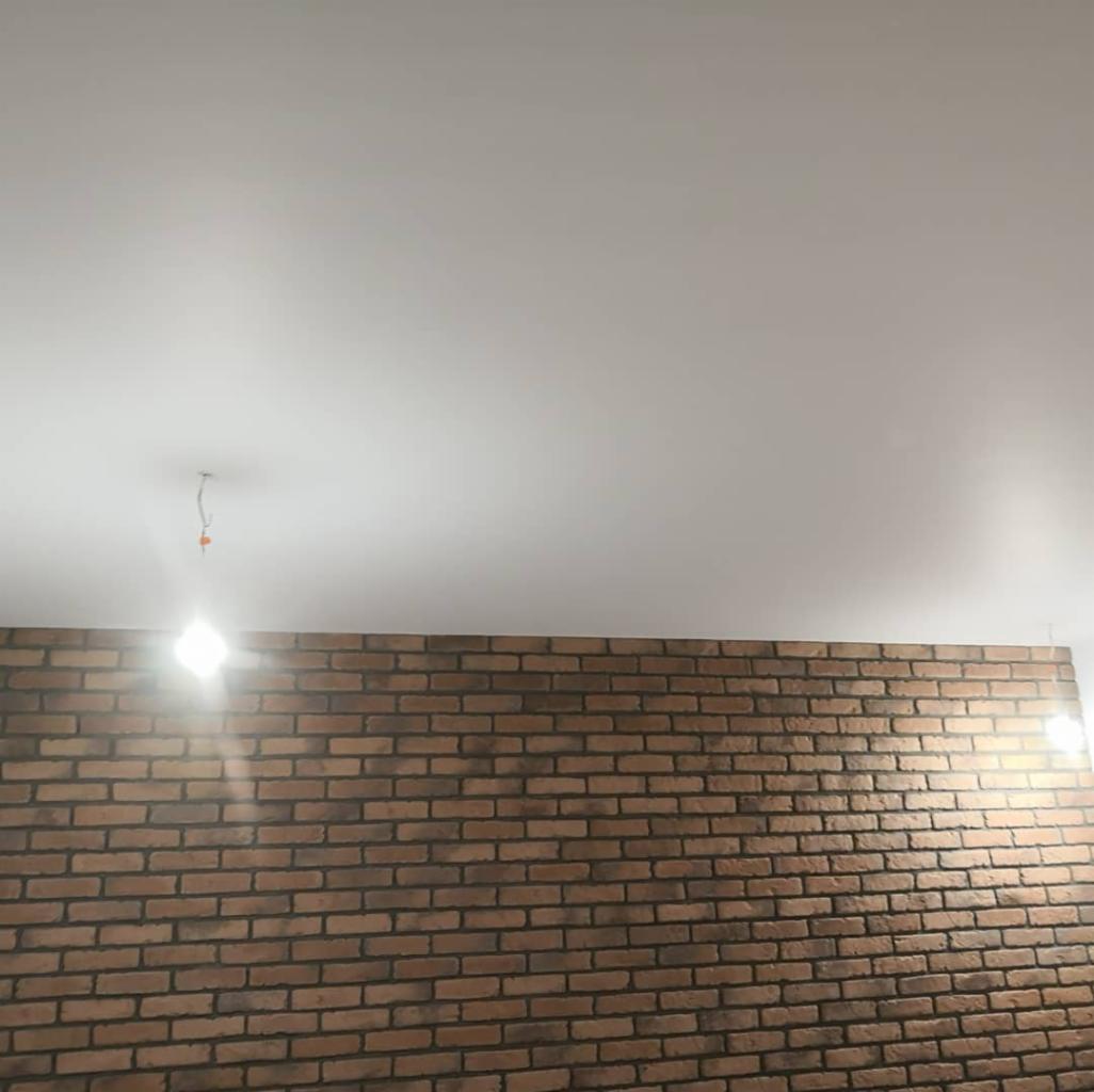Świeżo wykończona ściana z cegły dekoracyjnej w Zgierzu, z gładką, białą powierzchnią sufitu i wystającym kablem od lampy.