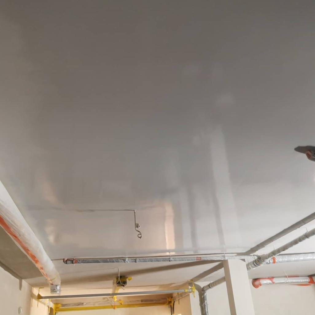 Gładka, szara powierzchnia sufitu po nałożeniu gładzi, widoczne instalacje zabezpieczone folią ochronną.