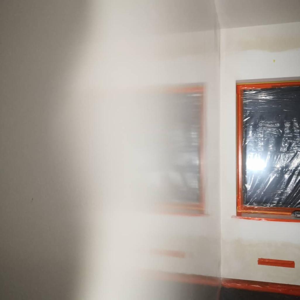 Przygotowanie do prac wykończeniowych: zabezpieczone okno folią ochronną i świeżo zagruntowana ściana z widocznymi śladami szpachlowania.