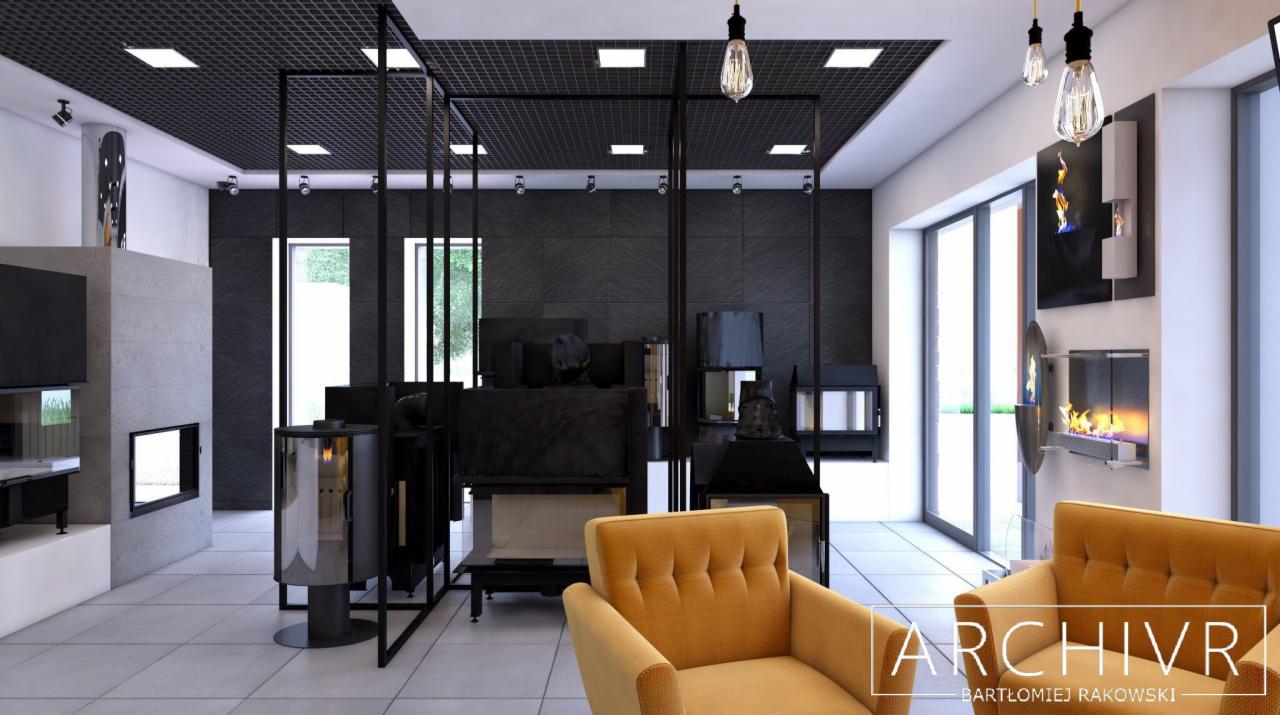 Salon z ekspozycją nowoczesnych kominków, oświetlony wiszącymi żarówkami i lampami LED, z żółtymi fotelami na pierwszym planie i logo projektanta w prawym dolnym rogu.