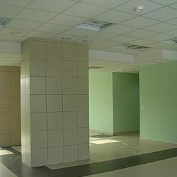 PHU MARBUD Marek Michaluk - Wnętrze komercyjne z kolumnami wyłożonymi jasnymi płytkami ceramicznymi, zielonymi ścianami i podwieszanym sufitem kasetonowym.