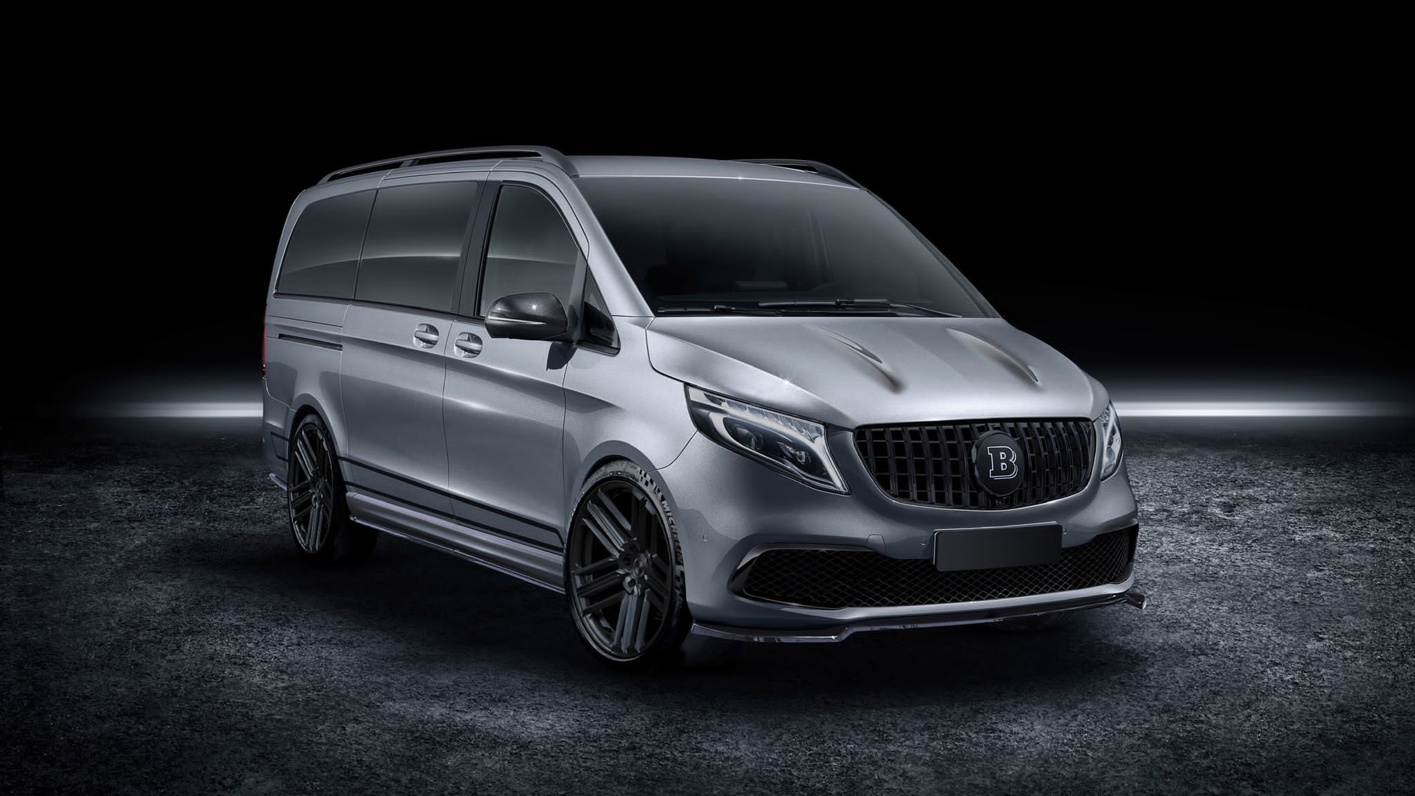 Szary, zmodyfikowany van z czarnymi felgami i grillem z logo 'B' w Wojkowicach, prezentowany na ciemnym tle.