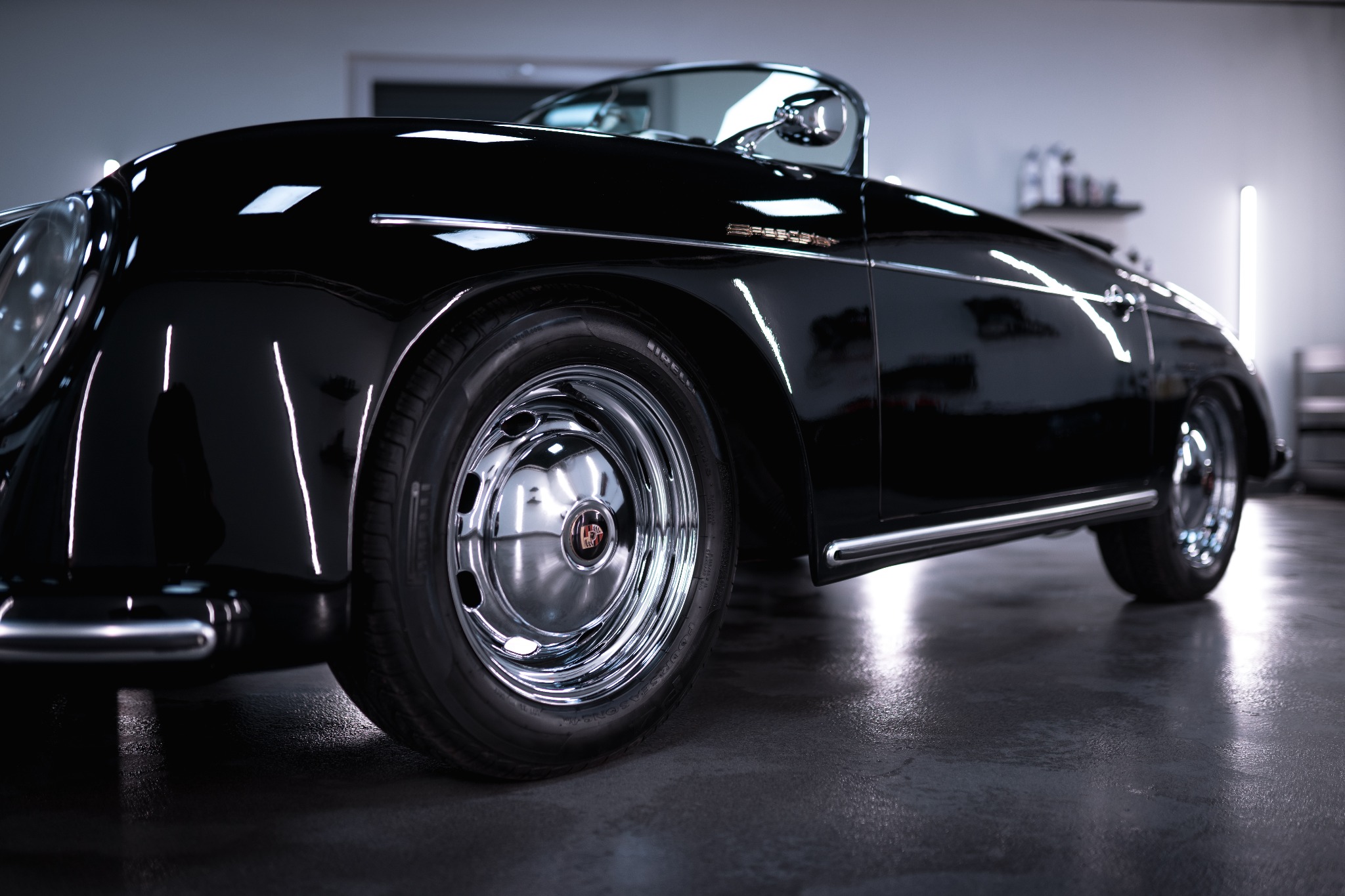 Błyszczący, czarny Porsche Speedster po renowacji, z chromowanymi felgami i detalami, sfotografowany w studio z reflektorami odbijającymi się w lakierze.