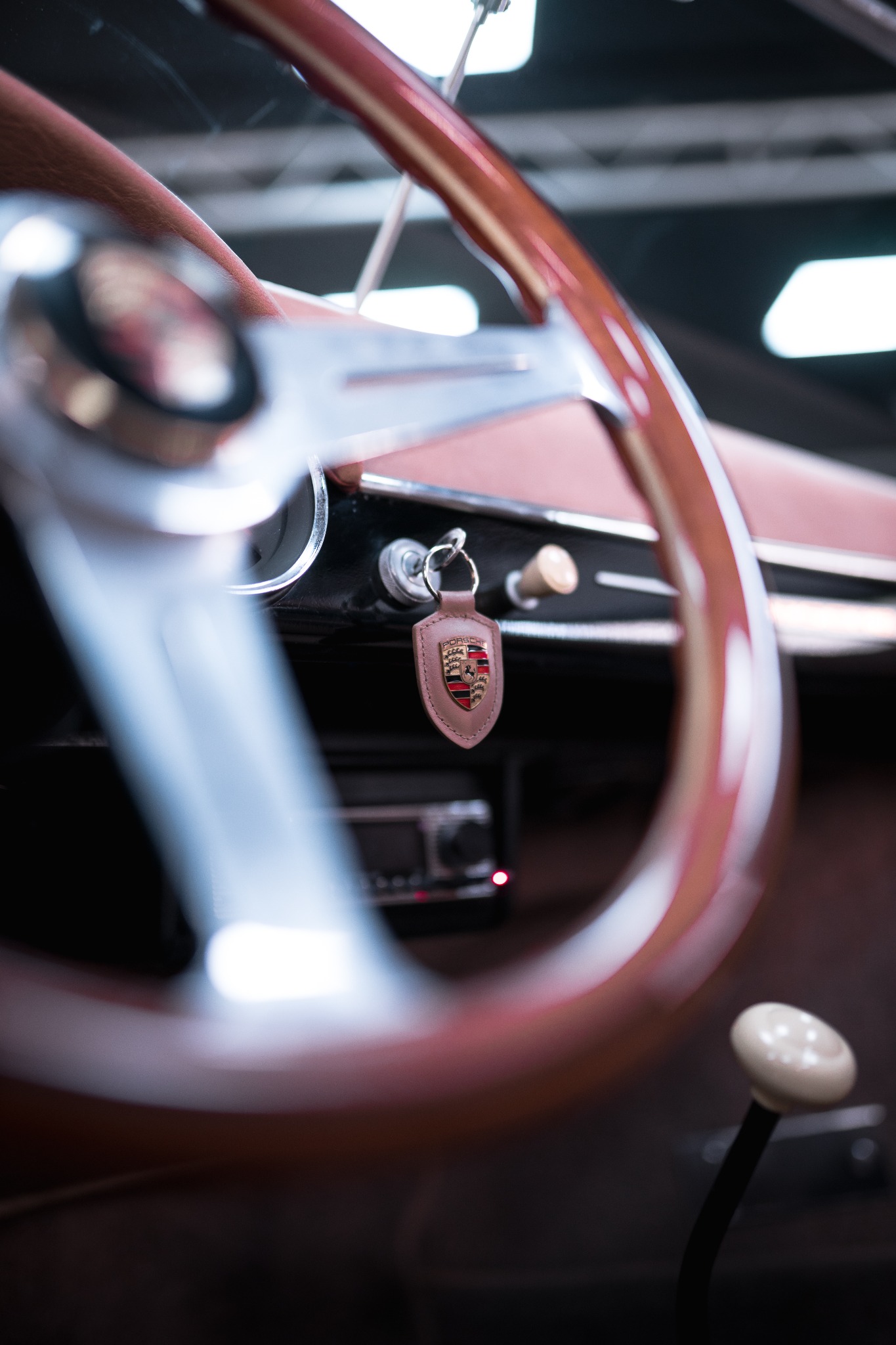 Wnętrze klasycznego Porsche Speedster z drewnianą kierownicą, skórzanym brelokiem z herbem Porsche przy kluczykach i gałką zmiany biegów w stylu retro.