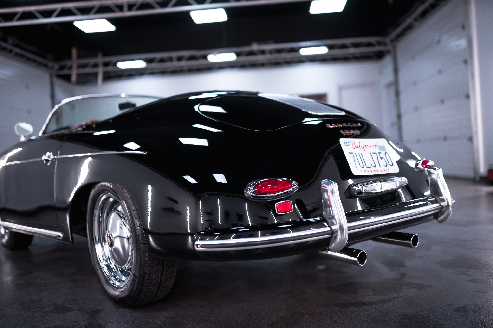 Czarny, odrestaurowany Porsche Speedster z widoczną tablicą rejestracyjną California, chromowanymi elementami i podwójnym wydechem, sfotografowany w dobrze oświetlonym garażu.
