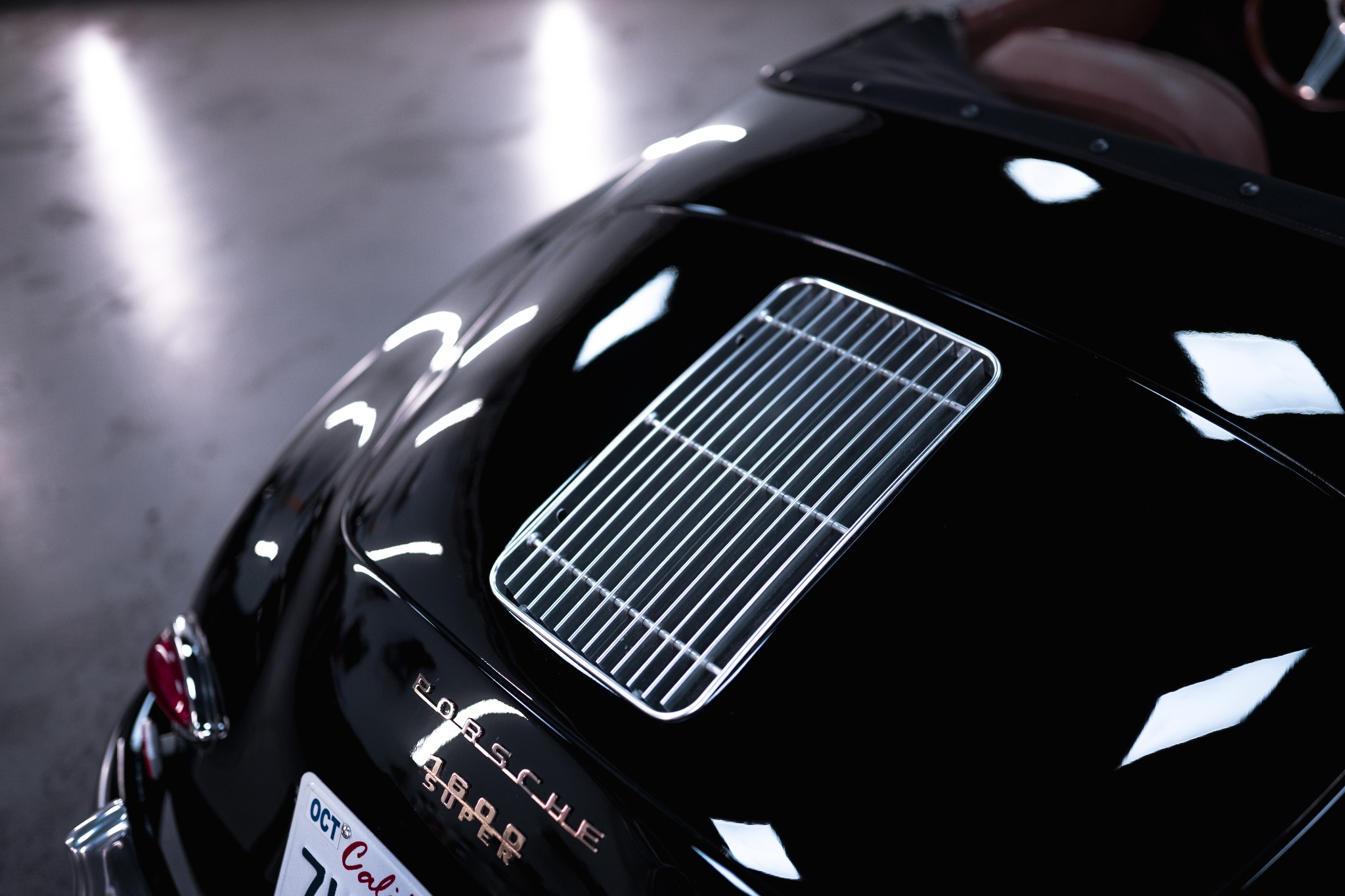 Błyszczący, czarny Porsche Speedster 1600 Super z chromowaną kratką wentylacyjną na tylnej klapie, widoczna tablica rejestracyjna z Kalifornii i fragment czerwonej lampy.