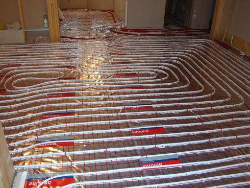 Rozłożona instalacja ogrzewania podłogowego z rurkami grzewczymi ułożonymi w pętle na folii izolacyjnej z siatką, przygotowana do zalania wylewką.