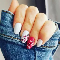 Dłoń z owalnymi paznokciami: dwa białe, jeden różowy i jeden biały z motywem kwitnącej wiśni, na tle dżinsowej kurtki.