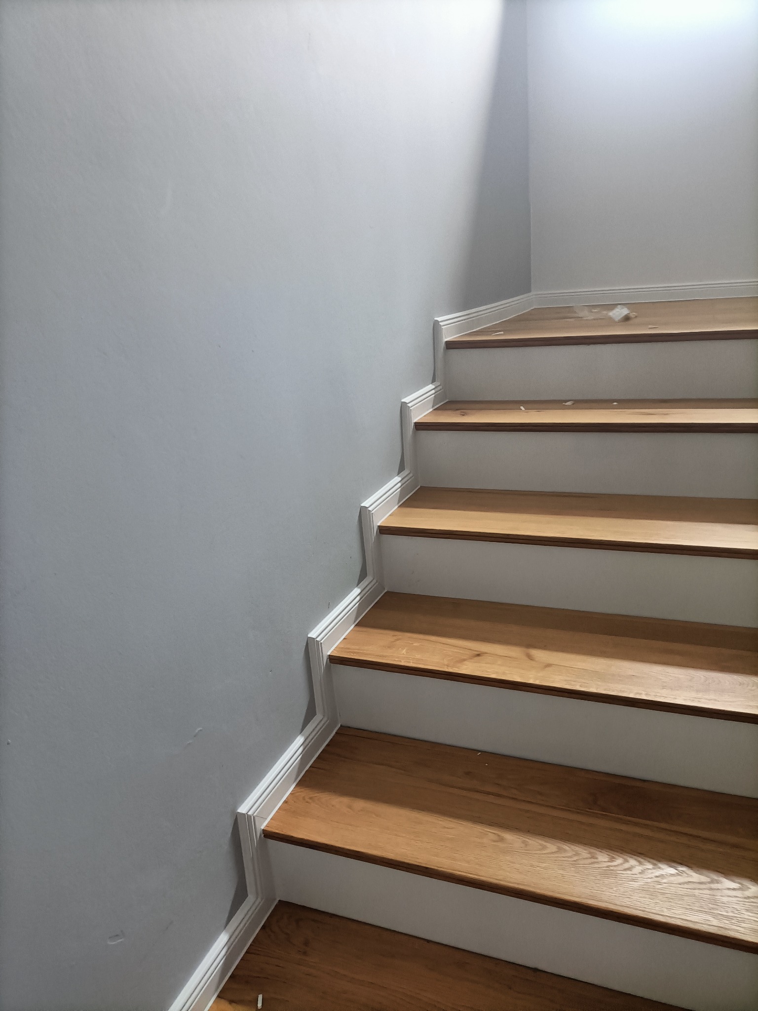Schody drewniane z białymi podstopnicami i listwami przypodłogowymi, świeżo po renowacji, z drobnymi zabrudzeniami na górnym stopniu.