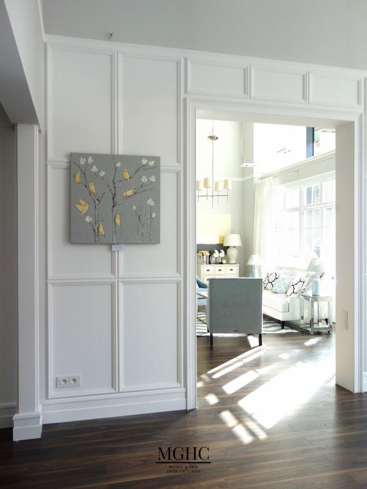 Wykończenie wnętrza restauracji: widok na salon przez ozdobne, białe drzwi z obrazem z motywem drzewa i ptaków na ścianie, ciemna drewniana podłoga z refleksami światła.