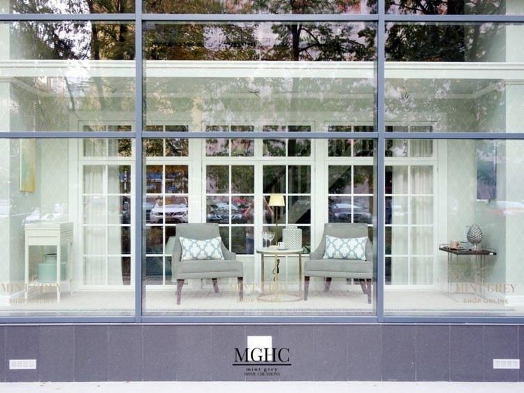 Witryna restauracji Mint Grey w Warszawie, widok z zewnątrz, z szarymi fotelami z wzorzystymi poduszkami, stolikami i dekoracjami wewnątrz, odbicie ulicy w szybach.