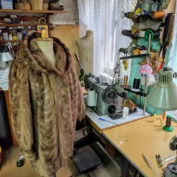 Futro z kapturem na manekinie w pracowni, w tle maszyna do szycia, nici i narzędzia.