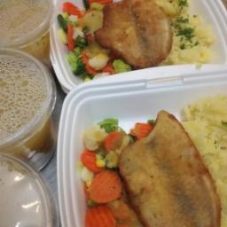 Restauracja Domek Smaków - Dwa białe pojemniki styropianowe z obiadem: smażona ryba, ziemniaki purée posypane koperkiem i mieszanka gotowanych warzyw, obok trzy pojemniki z zupą.