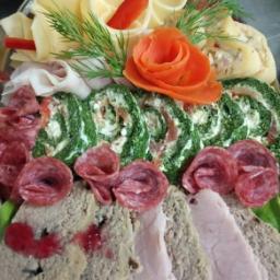 Restauracja Domek Smaków - Dekoracyjna zimna płyta z roladkami szpinakowymi, serowymi i z szynką, ozdobiona rozetą z marchewki i gałązkami kopru.