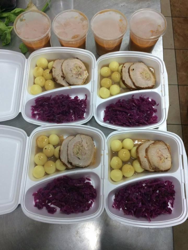 Cztery białe pudełka z gotowym obiadem: pieczone mięso z farszem, gotowane ziemniaki i duszona czerwona kapusta, plus cztery kubki z zupą krem.