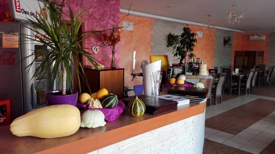 Wnętrze restauracji z dekoracjami z dyń na barze, widoczny dystrybutor piwa, stoliki i krzesła w tle