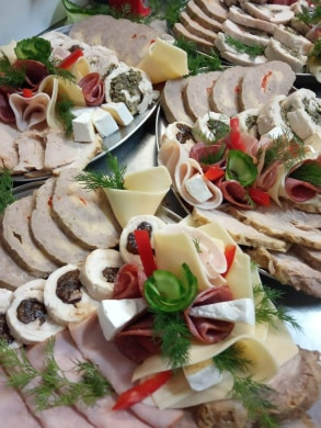 Dekoracyjna zimna płyta z wędlinami, serami i roladami, ozdobiona świeżym koperkiem i papryką na srebrnej tacy.