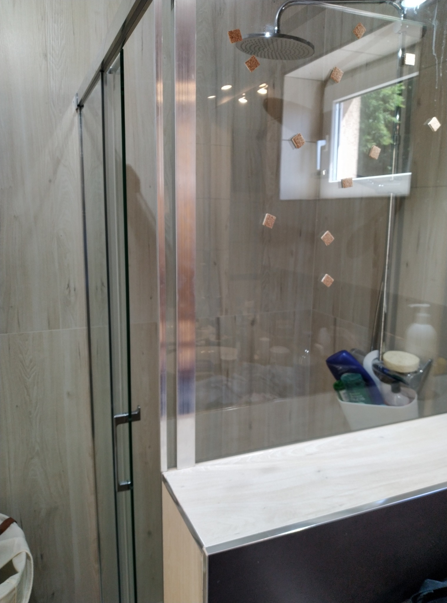 Nowoczesna kabina prysznicowa z przesuwnymi drzwiami, widoczne płytki imitujące drewno oraz akcesoria łazienkowe w koszyku.