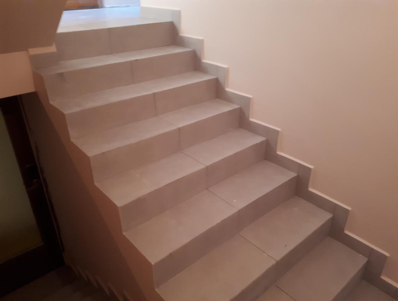 Wyłożone jasnymi płytkami schody wewnętrzne, widok z dołu, z widocznym fragmentem drzwi po lewej stronie.