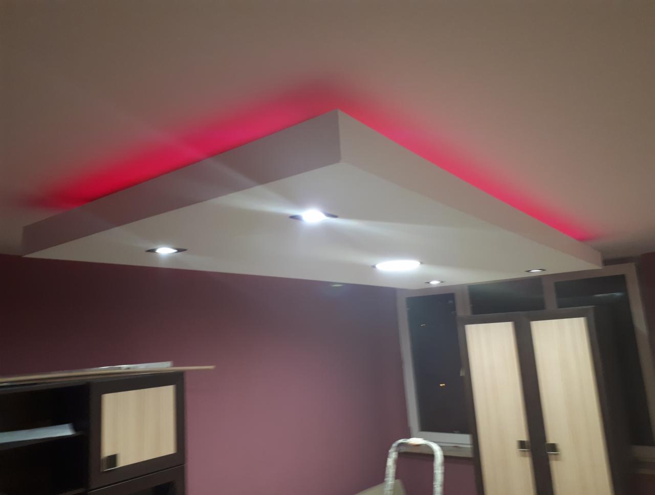 Nowoczesny sufit podwieszany z oświetleniem LED w kolorze czerwonym, w tle ściana w kolorze burgundowym oraz częściowo widoczna szafa.
