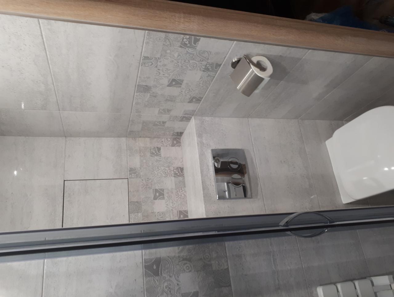 Wykończona łazienka z szarymi, wzorzystymi płytkami, ukrytym zbiornikiem toaletowym i metalowym uchwytem na papier toaletowy.