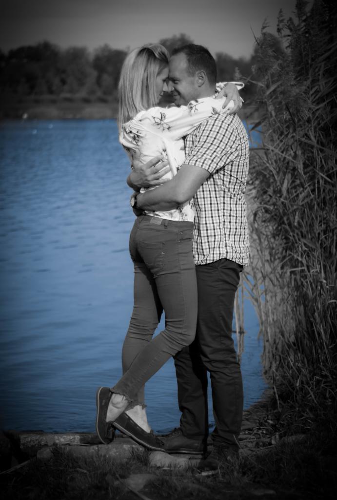 Para obejmująca się na tle jeziora, z efektem selektywnej kolorystyki uwydatniającym błękit wody.