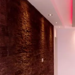 Ściana wykończona brązową okładziną imitującą cegłę w Konstantynowie Łódzkim, oświetlona punktowymi lampami w suficie podwieszanym z dekoracyjnym, czerwonym oświetleniem LED.