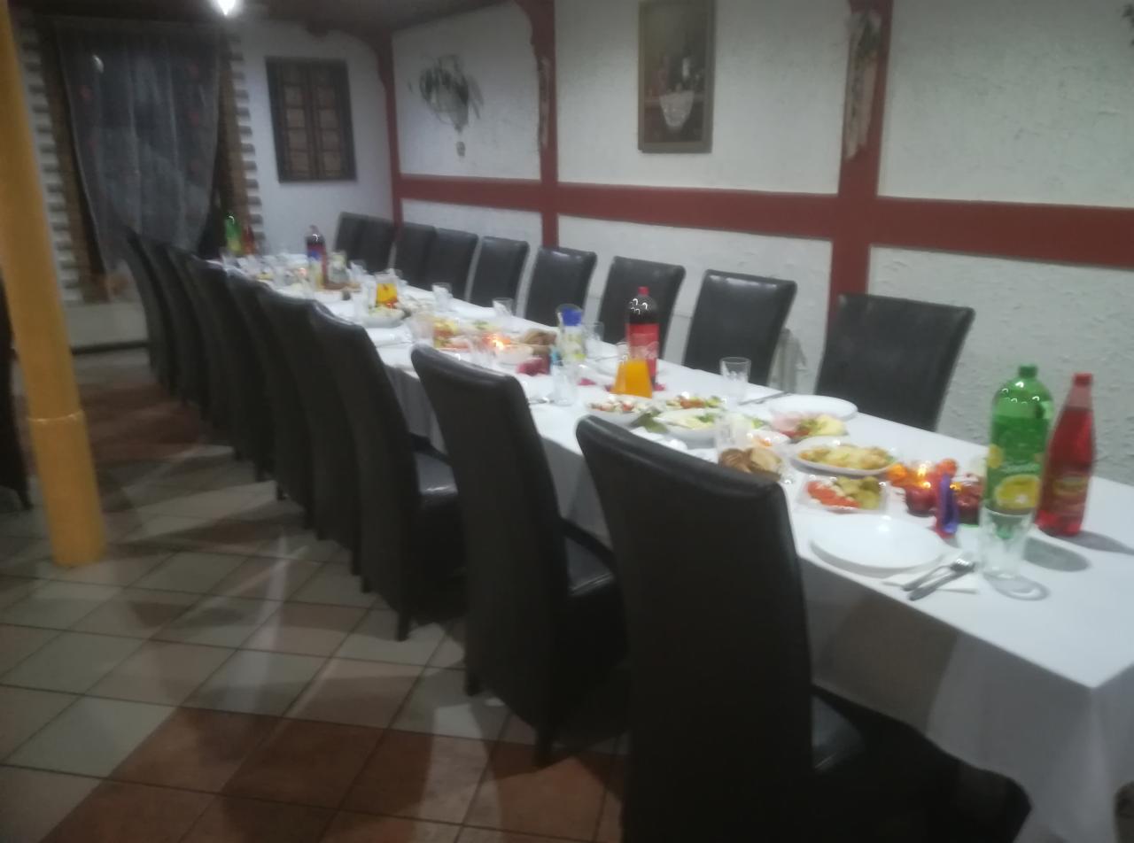 Długi stół nakryty białym obrusem, zastawiony naczyniami, potrawami i napojami w restauracji, ustawiony dla dużej grupy osób, z rzędem krzeseł z wysokim oparciem