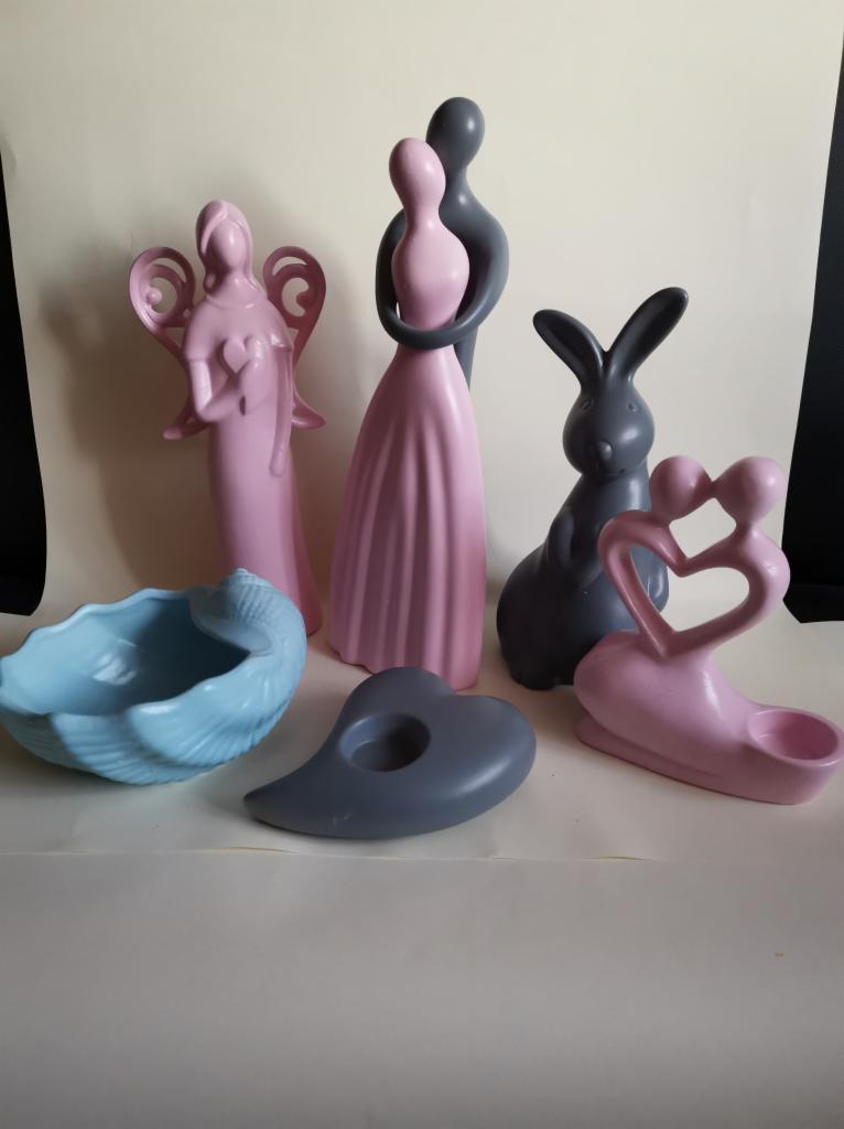 Różowe i szare figurki dekoracyjne: anioł ze skrzydłami, para w objęciach, zając oraz muszla i świecznik w kształcie serca, na białym tle.