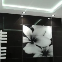 Nowoczesna łazienka z czarno-białymi błyszczącymi płytkami, motywem kwiatowym na ścianie, designerskim grzejnikiem drabinkowym i oświetleniem sufitowym.