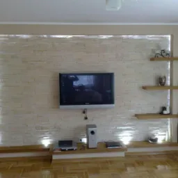 Ściana telewizyjna z dekoracyjną cegłą, podświetleniem LED, drewnianymi półkami i parkietem w jodełkę.