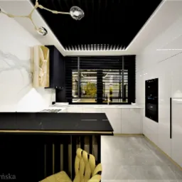 Nowoczesna kuchnia z czarno-białymi szafkami, złotymi akcentami i marmurową ścianą, oświetlona designerską lampą i naturalnym światłem z okna.